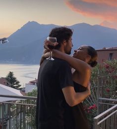 a man and woman standing next to each other on a balcony with mountains in the background