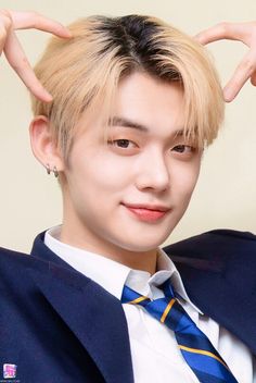 a young man with blonde hair wearing a blue suit and tie, holding his hands behind his head