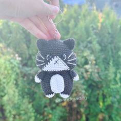 a crocheted cat ornament hanging from a string in front of some bushes