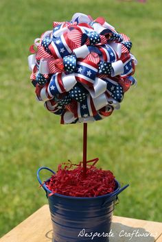 a red, white and blue pinwheel tree in a pail on a picnic table