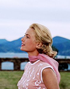 a woman standing in the grass with a frisbee on her hand and mountains in the background