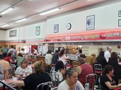 many people are sitting at tables in a restaurant with red and white walls, eating food