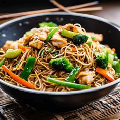 a bowl filled with noodles and vegetables on top of a table next to chopsticks