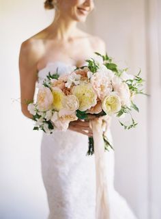 a woman in a wedding dress holding a bridal bouquet with white and yellow flowers