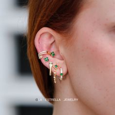 a close up of a person wearing ear rings with emeralds on them and gold chains