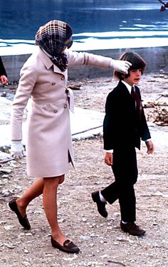 a woman in a trench coat and hat walking next to a young boy wearing black shoes