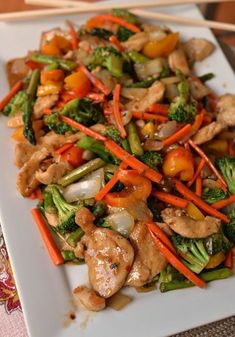 a white plate topped with chicken and veggies next to chopsticks on a table