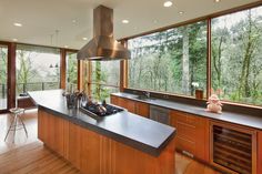 a kitchen with wooden cabinets and an island in front of large windows overlooking the woods