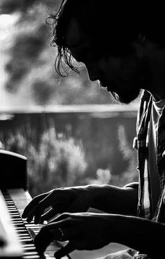 a man sitting at a piano in front of a window and playing the piano with his hands