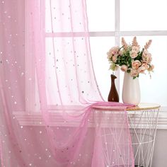 a vase filled with flowers sitting next to a window covered in pink sheers and stars