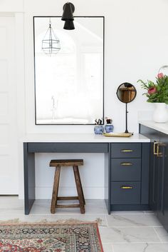 a desk with a mirror, stool and rug in a room that has white walls