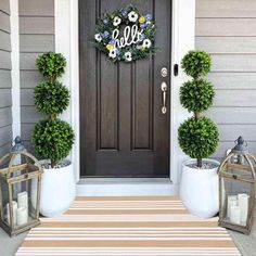 a front door decorated with two potted plants and a monogrammed welcome sign