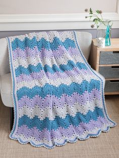 a blue and purple crocheted blanket sitting on top of a couch next to a white chair