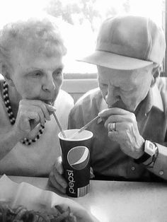 two older people sitting at a table eating food and drinking soda from a paper cup