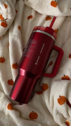 a red travel mug sitting on top of a white blanket