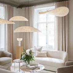 a living room filled with white furniture and lots of lights hanging from the ceiling above