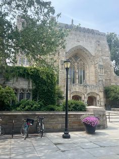 two bicycles are parked in front of a large stone building with ivy on the walls