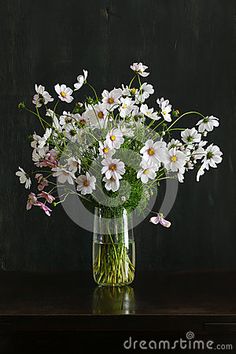 a vase filled with lots of white flowers on top of a wooden table next to a black wall