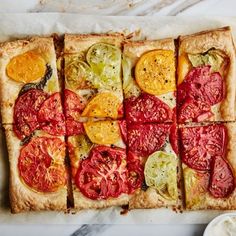 a square pizza with tomatoes and other toppings on top of parchment paper next to a bowl of sour cream