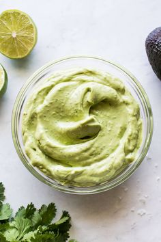 an avocado dip in a glass bowl surrounded by limes and cilantro