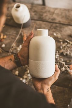 a person holding a white vase in their hand on a table with other items around it