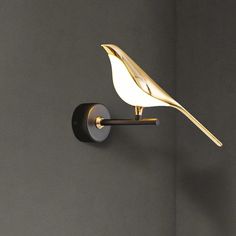 a white bird sitting on top of a wall mounted light next to a gray wall