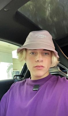 a woman sitting in the back seat of a car wearing a purple shirt and hat