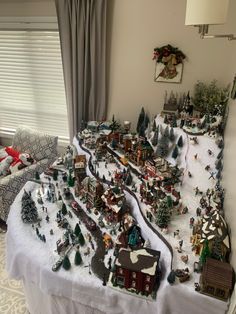 a christmas village is displayed on a table in front of a window with drapes