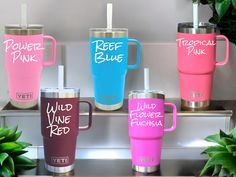 four different colored tumblers sitting on top of a shelf next to plants and potted plants