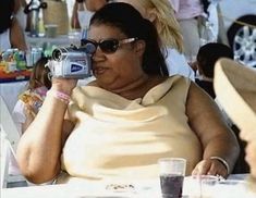 a woman sitting at a table talking on a cell phone while holding a camera up to her face