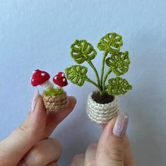 two tiny crocheted plants with leaves and mushrooms in them, one being held by a woman's hand