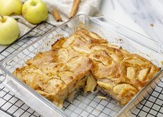 an apple pie in a glass baking dish on a cooling rack next to some apples