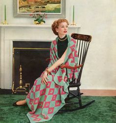 a woman sitting on a rocking chair in front of a fireplace with a blanket draped over her