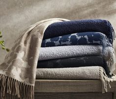 a stack of folded towels and blankets sitting on top of a wooden table next to a plant