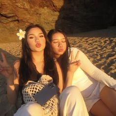 two women sitting on the beach making peace signs