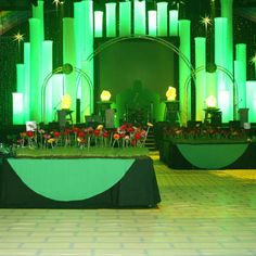 a stage set up for a party with green lighting and flowers in the center area