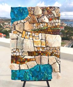 a piece of art made out of rocks and stones on top of a building with the ocean in the background