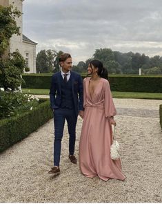 a man and woman walking in front of a large building with hedges on either side