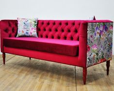 a red couch sitting on top of a hard wood floor next to a white wall