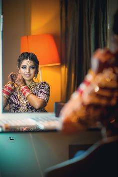 a woman sitting at a desk in front of a mirror with her hands on her face