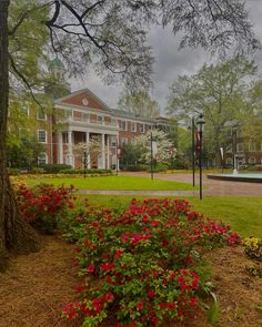 a red brick building sitting next to a lush green park filled with lots of flowers