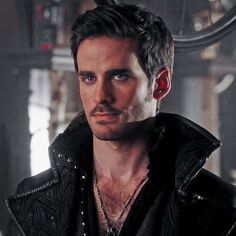 a man with dark hair wearing a black leather jacket and red earrings looking at the camera