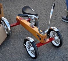 a wooden tricycle with black seat and chrome spokes is parked on the pavement