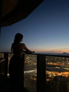 a woman standing on top of a tall building looking out at the city lights in the distance