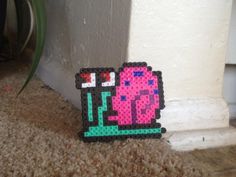 a small pixel art piece sitting on the floor next to a wall and potted plant