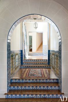 an arched doorway leads into a hallway with blue and white tiles on the walls, along with wooden steps