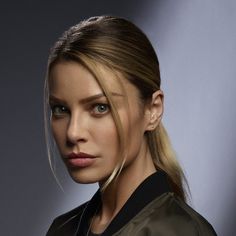 a woman with blond hair wearing a leather jacket and earring set in front of a gray background