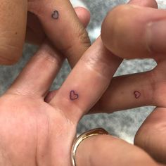 two people holding hands with small hearts tattooed on their thumbnails and finger rings