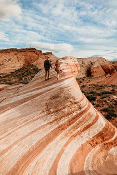 two people walking on the side of a large rock formation in the middle of nowhere