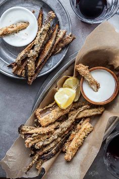 two plates filled with fried fish sticks next to cups and sauces on a table